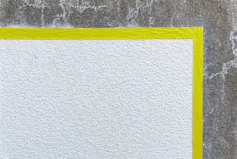 Gereinigte Probefläche von etwa 1 m², mit gelbem Klebeband auf einer verschmutzten Putzfassade markiert